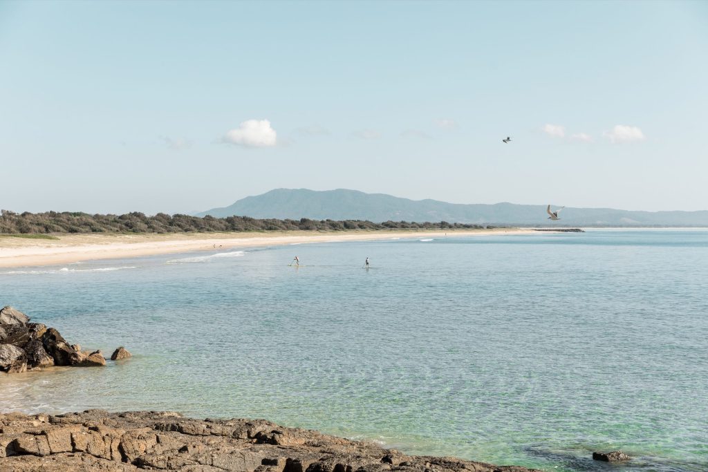scenic shot of beach and mountains in background, people paddle surfing on the flat water
